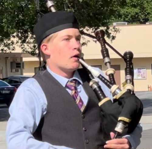 Logan Gorsuch playing bagpipes outdoors in a kilt